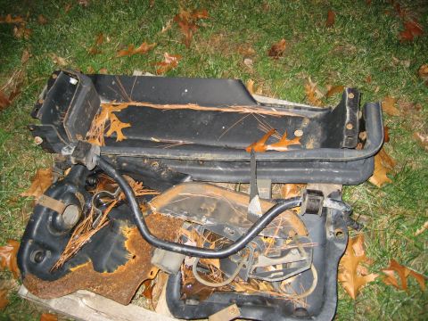 1996 Ford Bronco - Scattered car parts, some heavily rusted, lie on a patch of grass covered in fallen leaves.