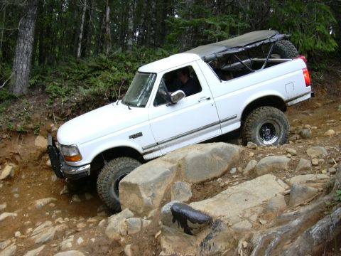 1991 Ford Bronco - 1991 Ford Bronco tackling a challenging off-road course with large rocks and dirt.