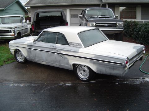 1964 Ford Fairlane - A 1963 Ford Falcon coupe in primer sits on a wet driveway, with other vehicles and a house in the background.