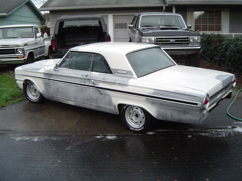 Mid-1960s Ford Fairlane hardtop in primer on steel wheels in a wet driveway