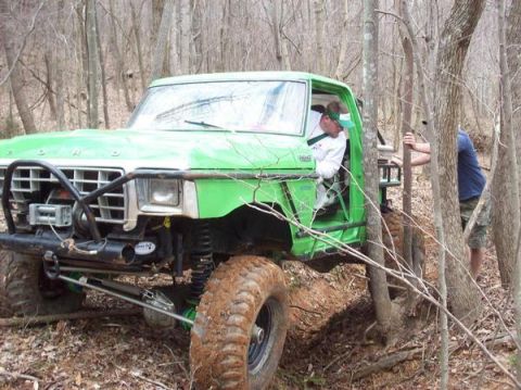 1978 Ford Bronco - Modified 1978 Ford Bronco navigating a wooded trail, showing significant suspension lift and off-road tires.
