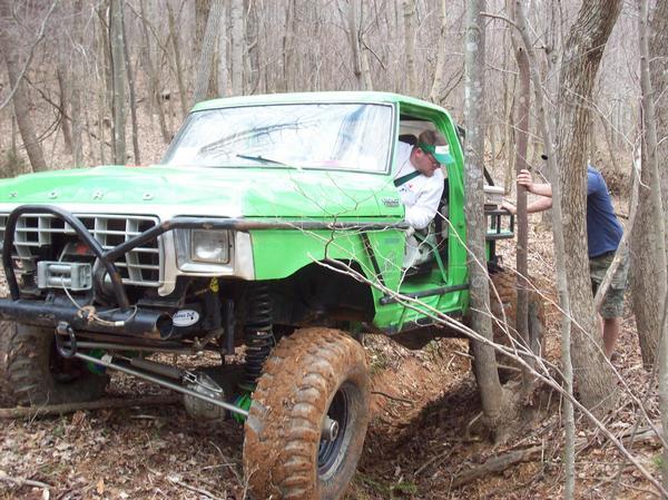 Green 1978 Ford Bronco modified for off-roading, stuck in woods with driver inside