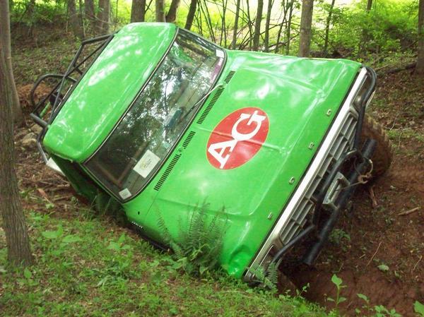 Green 1978 Ford Bronco tilted in a ditch with an AG logo on the hood