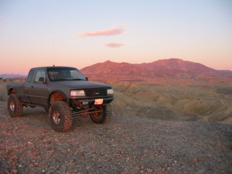 1997 Ford Ranger - This lifted pickup truck is parked on a rocky surface with mountains in the distance during sunset.