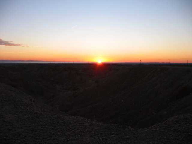Sunset over a barren landscape with a faint contrail in the sky