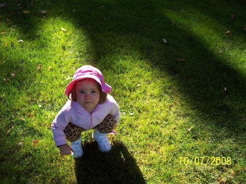 2000 Ford Crown Victoria - A young child in a pink hat and patterned pants crouches on a grassy lawn, with a date stamp visible in the corner.