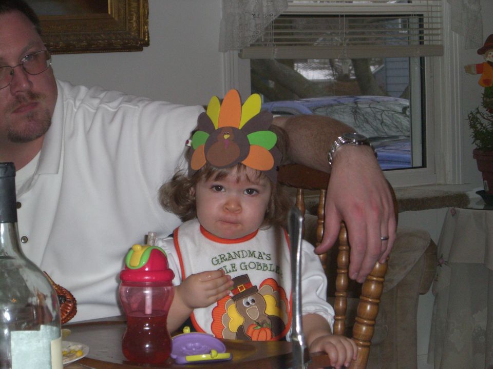 Child in a high chair wearing a turkey headband and bib that says "Grandma's Little Gobble"