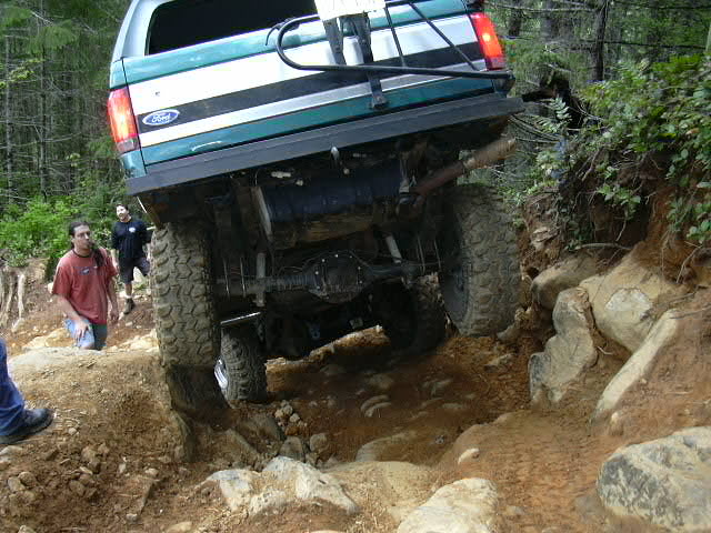 Rear underside of a lifted green Ford pickup articulating over rocks, driveline and rear axle exposed