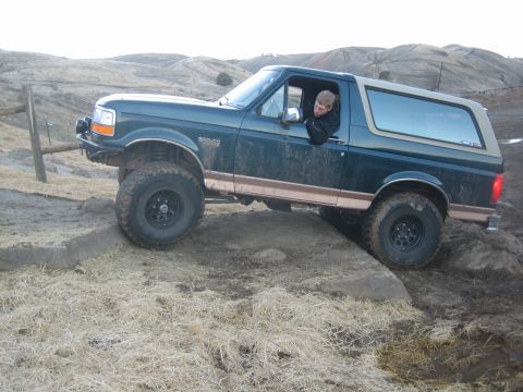 1995 Ford Bronco - A man drives a 1995 Ford Bronco over an obstacle on a dry, hilly terrain.