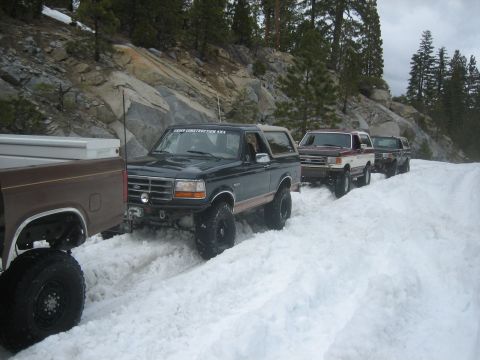 1995 Ford Bronco - A convoy of SUVs navigates a snow-covered mountain path, with one Bronco leading the way.