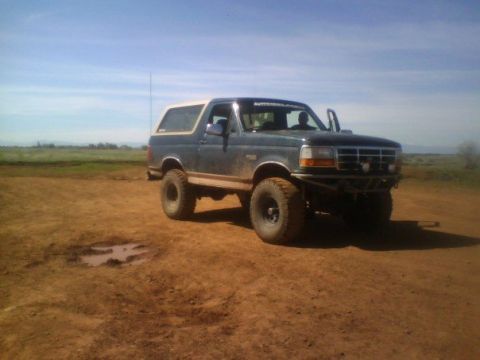 1995 Ford Bronco - A Ford Bronco sits on a dusty, open plain under a bright blue sky.