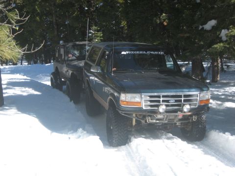 1995 Ford Bronco - A Ford Bronco and Jeep navigate a snowy path through a forest.