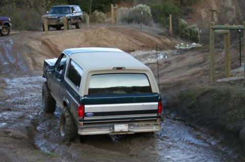 1995 Ford Bronco - A Ford Bronco navigates a muddy off-road trail with another SUV in the background.