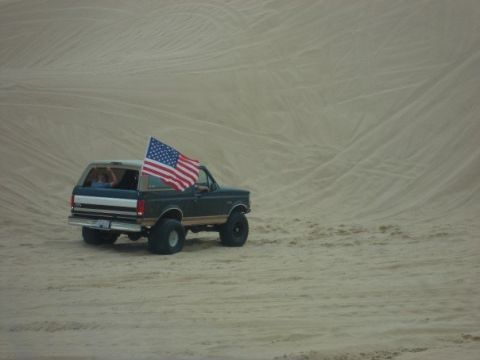 1995 Ford Bronco - A 1995 Ford Bronco flies an American flag while traversing sandy terrain.