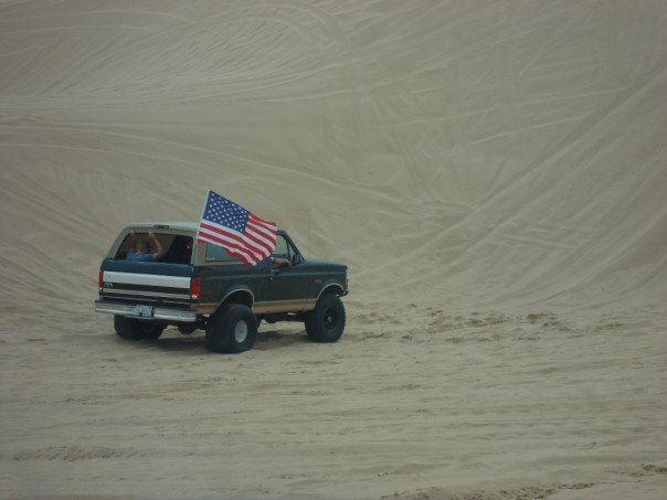 Dark green 1995 Ford Bronco with American flag driving on sand dunes