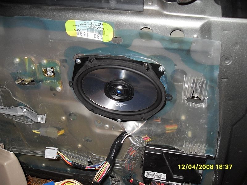 Car door interior panel removed, showing a speaker, wiring harness, and electronic module. Date stamp 12/04/2008