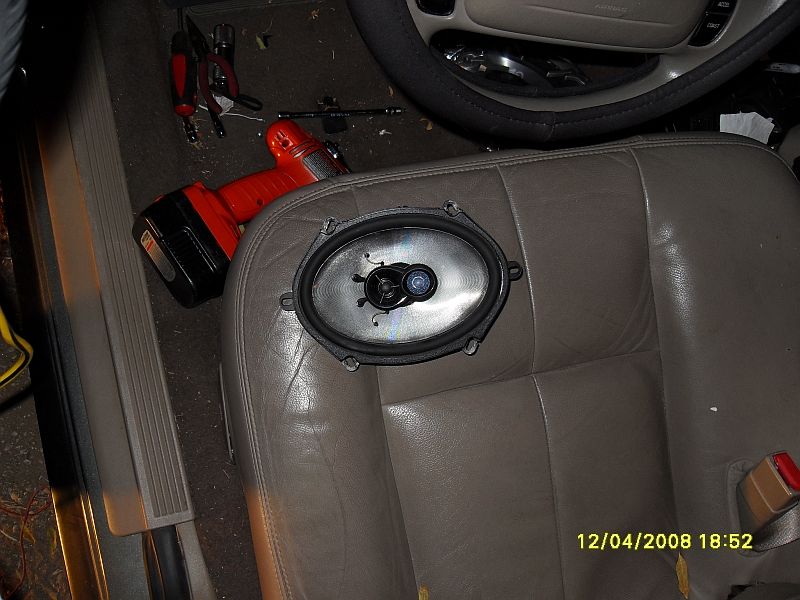 Aftermarket oval speaker on car seat next to drill and tools. Interior view.