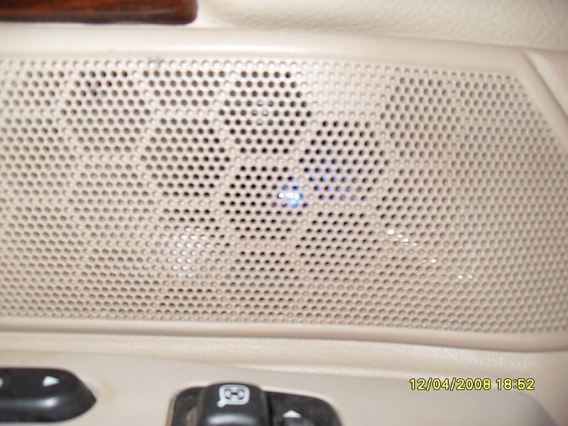 Car interior door panel speaker grille with blue light and window controls.