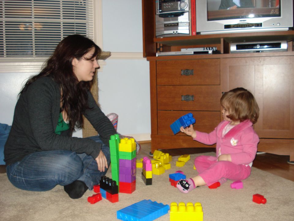 Woman and child playing with colorful building blocks on a carpeted floor