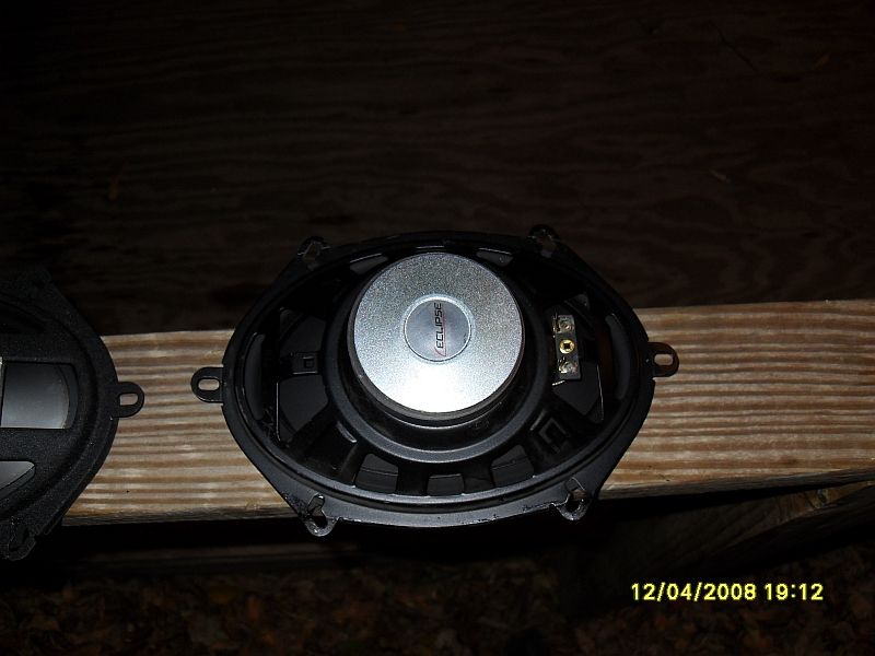 Two oval car speakers, one with an "ECLIPSE" logo, on a wooden surface.