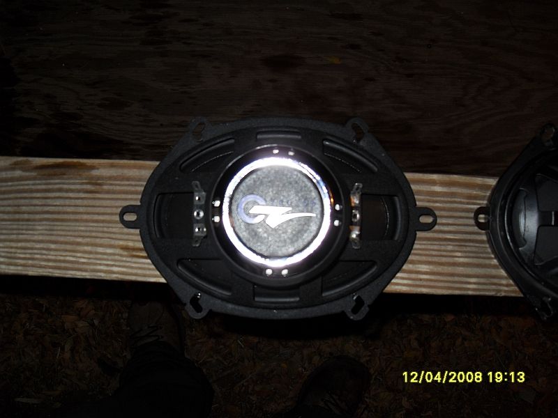 Two oval car speakers on a wooden surface, one with a GT logo.