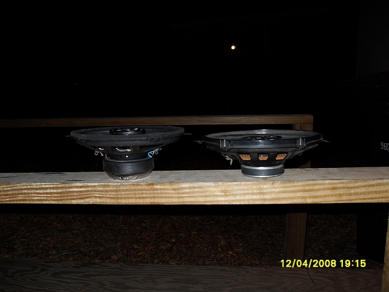 Two car speakers on a wooden plank at night.