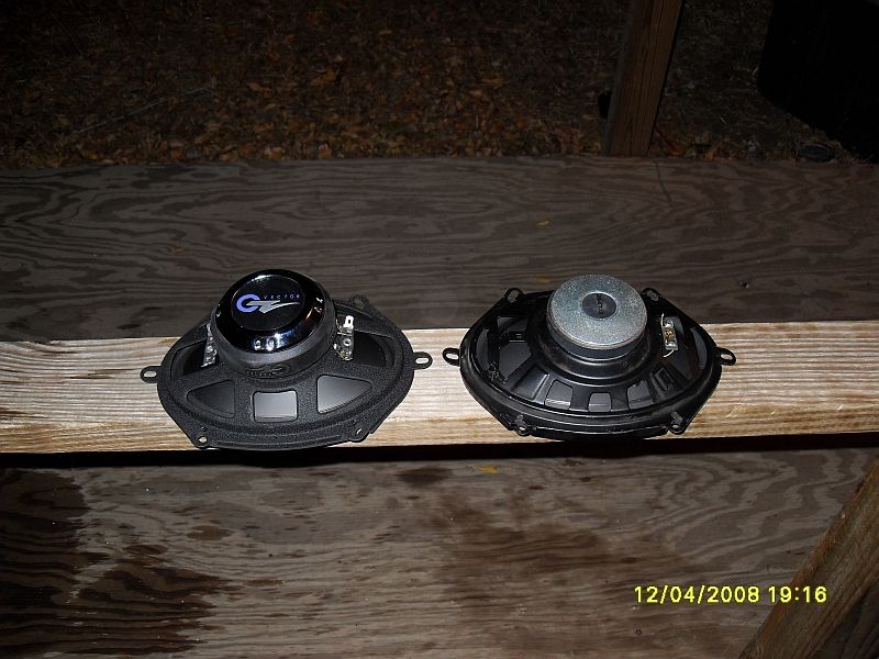 Two car speakers on a wooden surface, one with a blue and silver "G VECTOR" logo.
