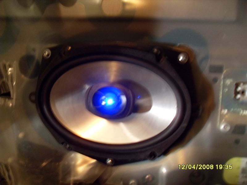 Aftermarket oval speaker with blue LED light in a car door panel.