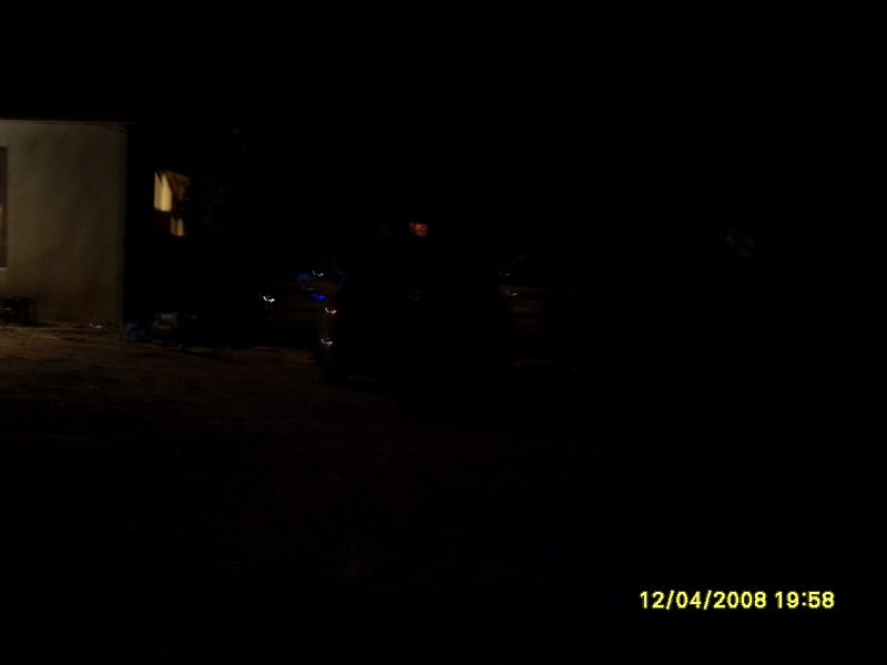 Dimly lit outdoor scene at night with a building and faint vehicle headlights.