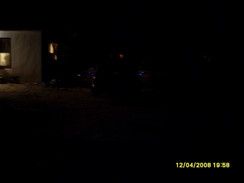 Dark sedan parked in front of a building at night, with faint blue lights visible.
