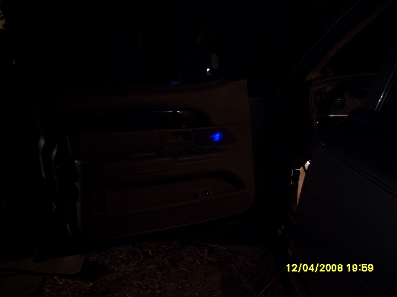 Car interior at night, driver's door panel with blue light, dashboard visible, timestamp.
