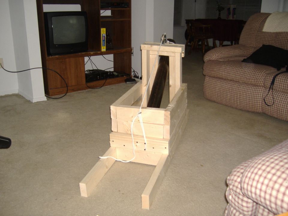 Wooden contraption on carpeted floor in front of TV stand and armchair.