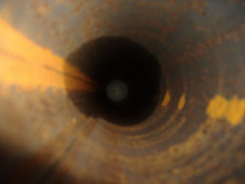 1988 Ford Bronco - A close-up, tunnel-vision view looking down the inside of a rusty, metallic pipe or exhaust system. Bright yellow light streaks in from the…