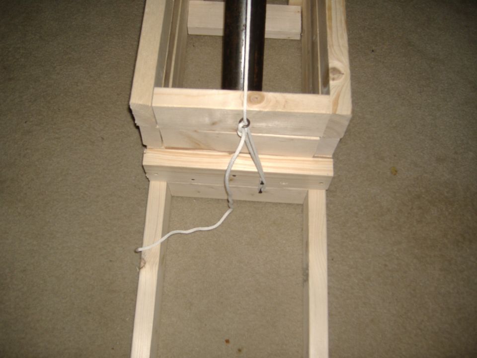 Homemade wooden stand with black steel tube and white cord tied to a screw eye, on carpet