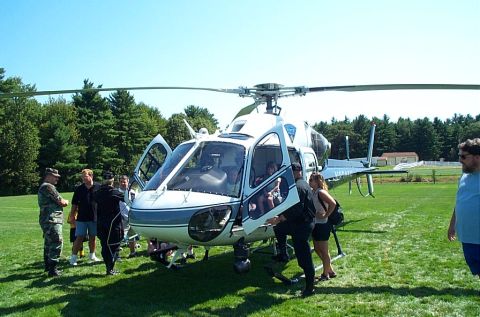1991 Ford LTD Crown Victoria - A white and blue helicopter sits on a grassy field with its doors open, surrounded by several people.