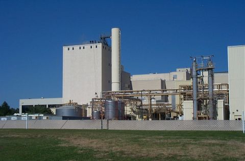 1991 Ford LTD Crown Victoria - A large industrial facility with multiple buildings, tanks, and a tall smokestack is seen on a clear day.