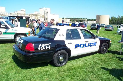 1991 Ford LTD Crown Victoria - A black and white police car is parked on the grass at an outdoor event, with other vehicles and people in the background.