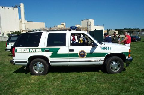 1991 Ford LTD Crown Victoria - A white Border Patrol SUV is parked on a grassy field with industrial buildings in the background.