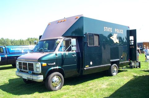 1991 Ford LTD Crown Victoria - Photograph of a green GMC State Police mobile command/box van on grass, not a technical document.