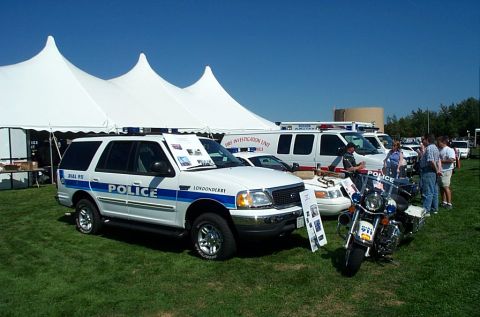 1991 Ford LTD Crown Victoria - Photograph of a white police SUV and emergency vehicles on display beside a large event tent.