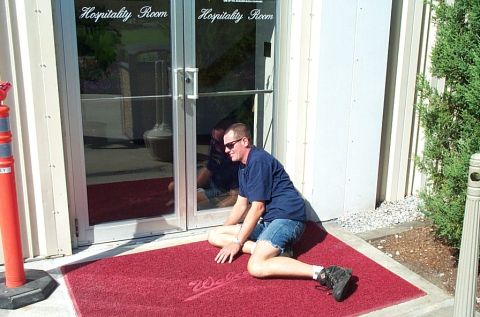 1991 Ford LTD Crown Victoria - Photograph of a man on a red welcome mat outside glass Hospitality Room doors.