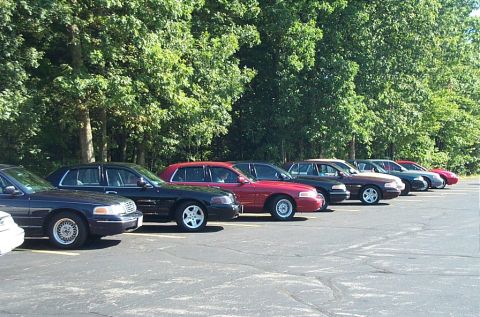 1991 Ford LTD Crown Victoria - Photograph of a row of parked cars at an outdoor meet, not a technical document.
