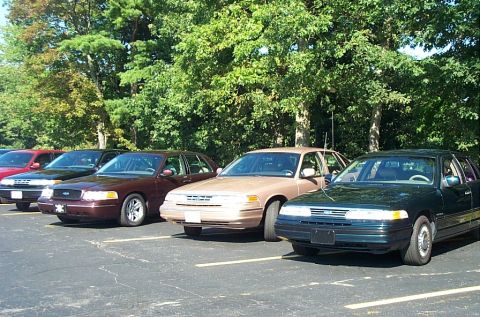 1991 Ford LTD Crown Victoria - Photograph of four parked Ford sedans in a tree-lined lot, not a technical document.