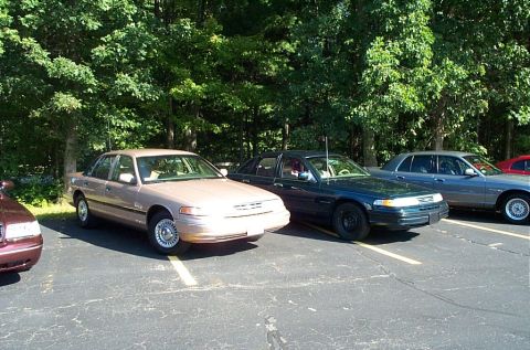 1991 Ford LTD Crown Victoria - Photograph of parked sedans along a tree line in a lot, not a technical document.