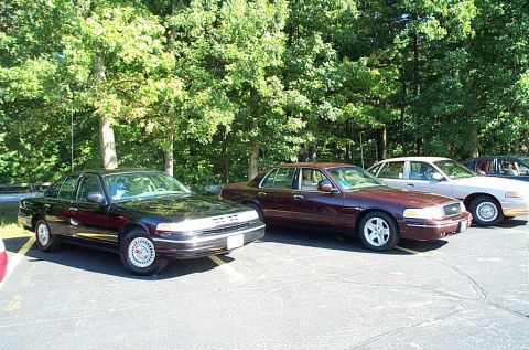 1991 Ford LTD Crown Victoria - Photograph of parked black and maroon sedans in a wooded lot, not a technical document.