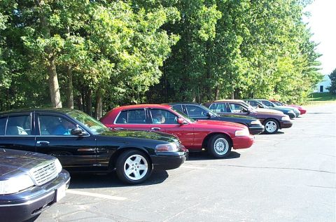 1991 Ford LTD Crown Victoria - Photograph of a curving row of parked cars beside trees, not a technical document.