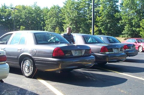 1991 Ford LTD Crown Victoria - Photograph of a person behind three parked sedans in a lot, not a technical document.