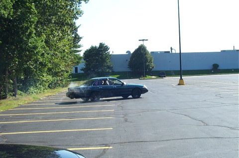 1991 Ford LTD Crown Victoria - Photograph of a dark sedan emitting exhaust in a parking lot, not a technical document.