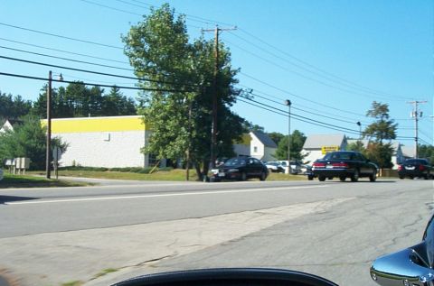1991 Ford LTD Crown Victoria - Photograph of a street with a yellow-and-white building and cars in a lot.