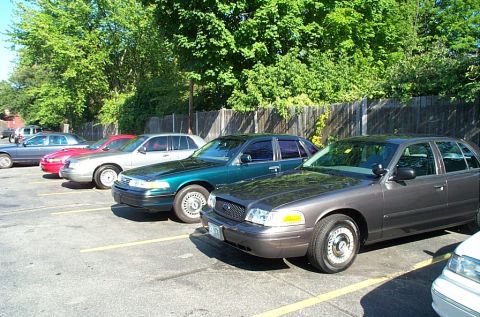 1991 Ford LTD Crown Victoria - Photograph of several full-size sedans parked in a row in a fenced lot.
